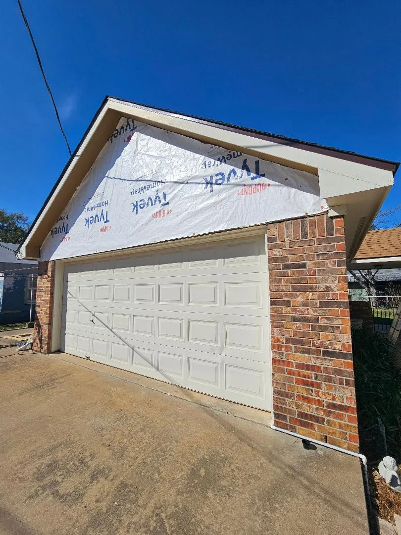 Roof sheathing with white underlayment on brick garage structure with white garage door