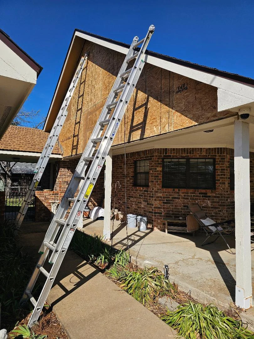Aluminum ladders securing plywood panels over damaged windows and openings on brick residential structure